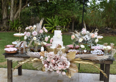 Rustic wedding dessert table with pastel roses, pampas grass, and elegant white tiered cake.
