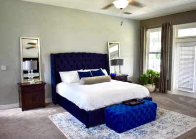 Elegant master bedroom at Saint Patrick Palace with navy tufted bed, velvet bench, and natural light in Davie, Florida