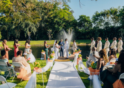Romantic lakeside wedding with fountain backdrop, white aisle, and colorful spring florals.