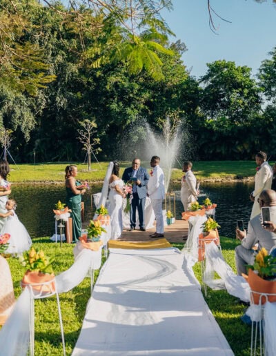 Romantic lakeside wedding with fountain backdrop, white aisle, and colorful spring florals.