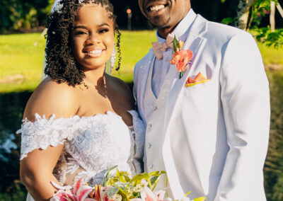 Bride and groom at Saint Patrick Palace with tropical bouquet and elegant white suit in a romantic outdoor setting.