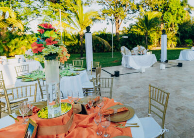 Vibrant outdoor wedding reception with tropical florals, gold chairs, and elegant table settings.