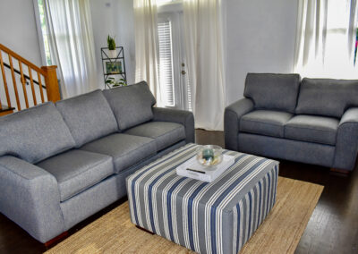 Guest cottage living room at Saint Patrick Palace with modern seating, striped ottoman, and natural light in Davie, Florida