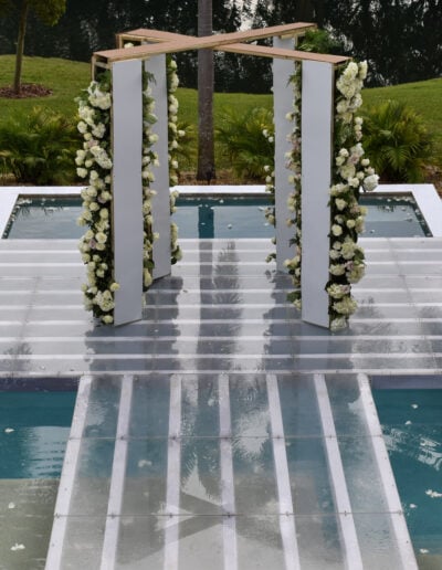 Floating glass wedding aisle with floral arch over the pool at Saint Patrick Palace.