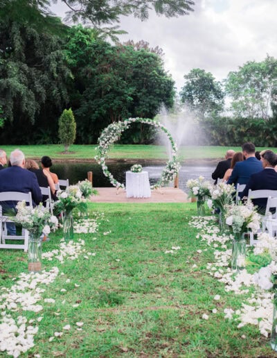 Lakeside wedding ceremony with circular floral arch at Saint Patrick Palace in Davie, FL.