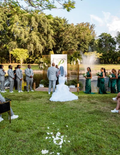 Lakeside outdoor wedding ceremony with custom altar and emerald bridal party at Saint Patrick Palace in Florida.