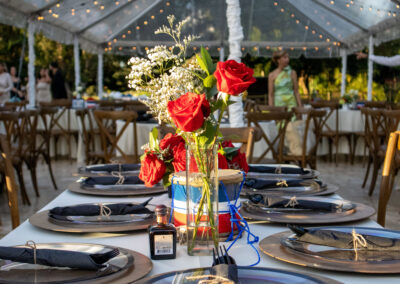 Rustic outdoor reception with red rose centerpieces, twinkle lights, and wooden accents at Saint Patrick Palace.