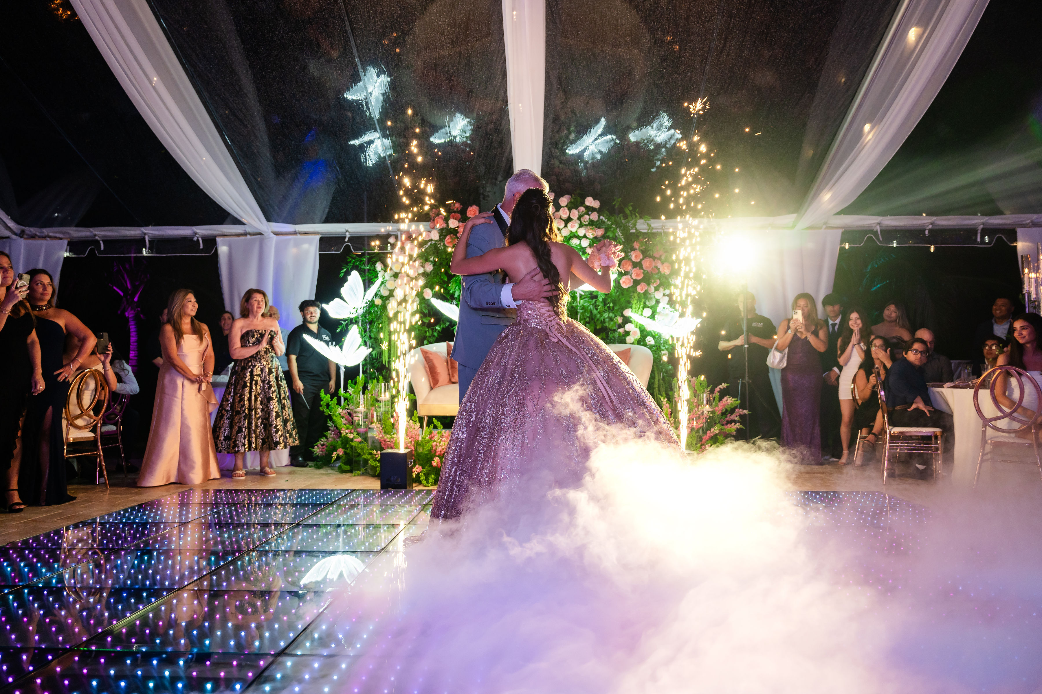 Rose gold quinceañera first dance with sparklers and fog under a 40x80 clear-top tent at Saint Patrick Palace.