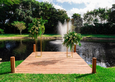 Lakeside wedding dock with lush floral decor and fountain backdrop for a romantic ceremony setting.