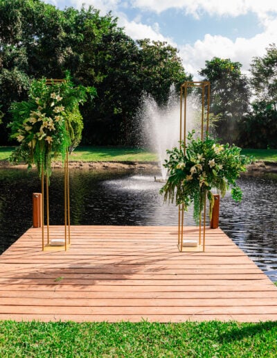 Lakeside wedding dock with lush floral decor and fountain backdrop for a romantic ceremony setting.