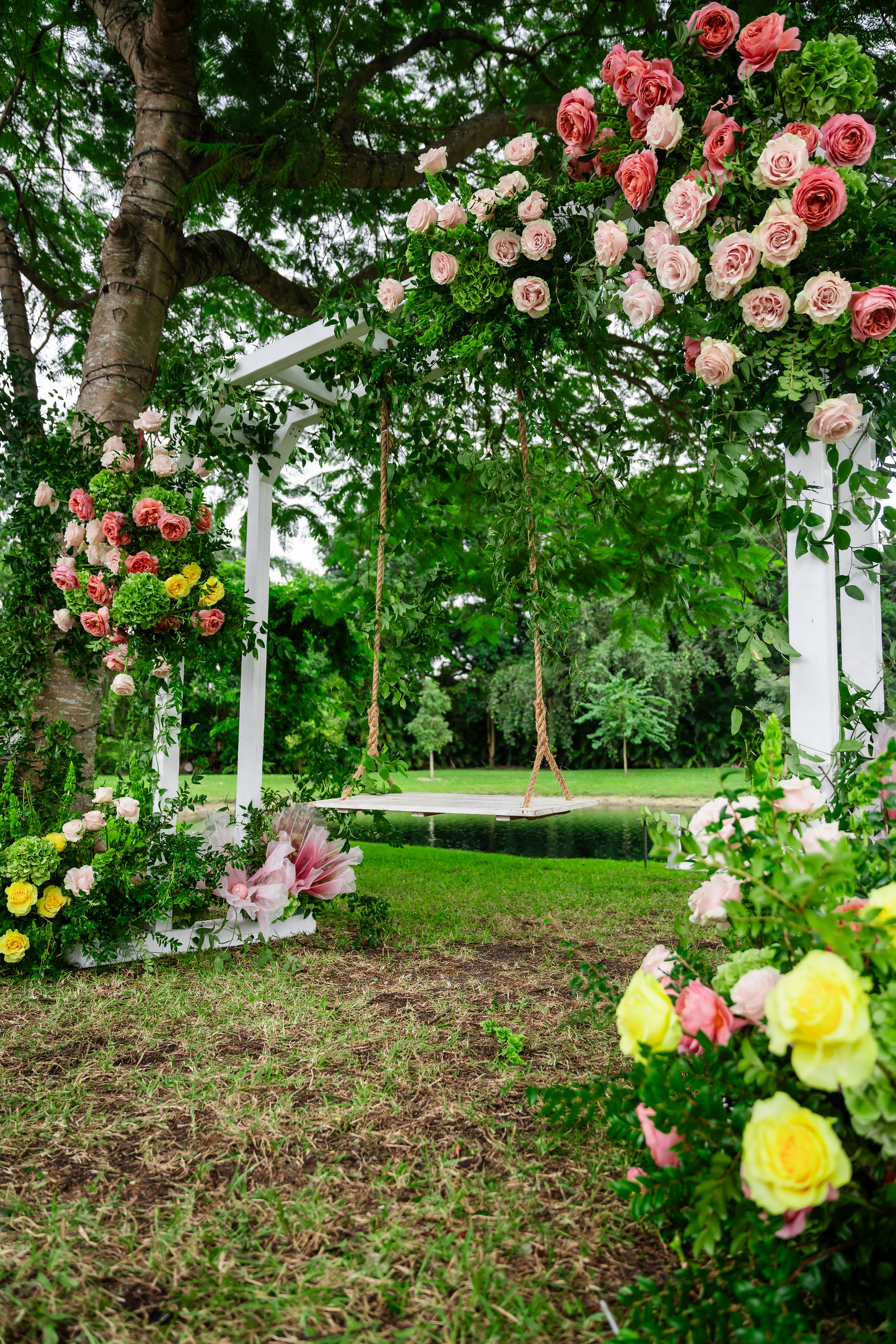Rose gold quinceañera album setting with a floral swing frame and pond backdrop at Saint Patrick Palace estate gardens.