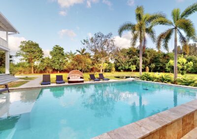 Resort-style pool at Saint Patrick Palace with travertine deck, palm trees, and lounge seating in Davie, Florida
