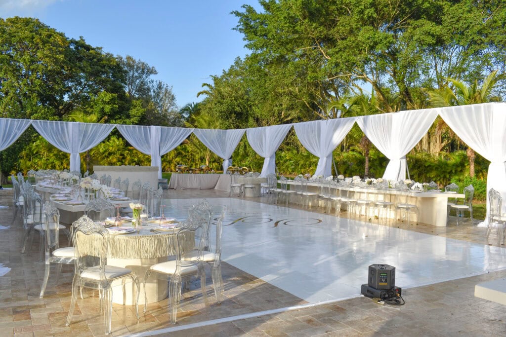 Elegant outdoor wedding with white draping, luxe decor, and a glossy dance floor.