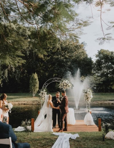 Romantic lakeside wedding with fountain backdrop and white floral arch at Saint Patrick Palace.
