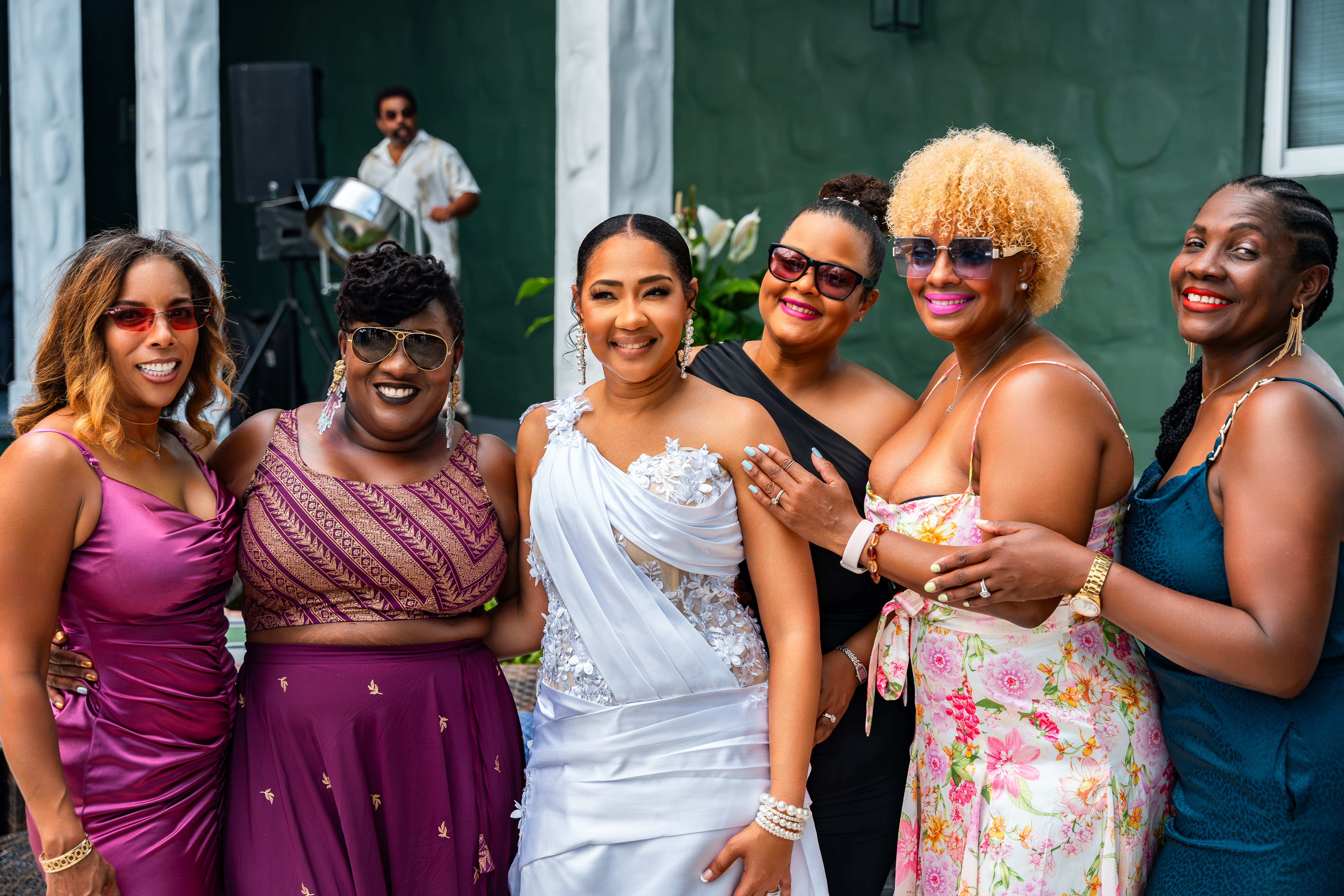 Bride with friends posing during cocktail hour with a steel drum player performing in the background at Saint Patrick Palace.