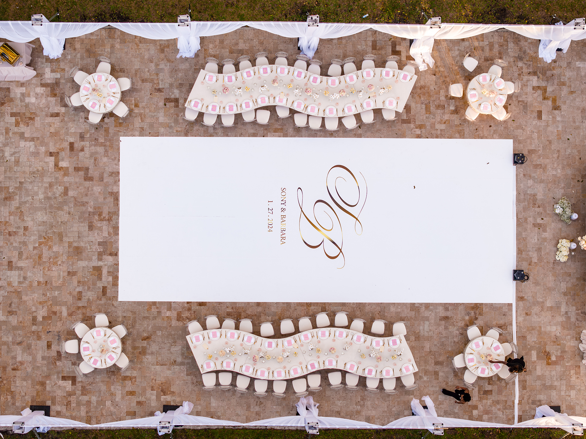 Aerial view of an outdoor wedding reception at Saint Patrick Palace with a custom white monogram dance floor and elegant table layout.