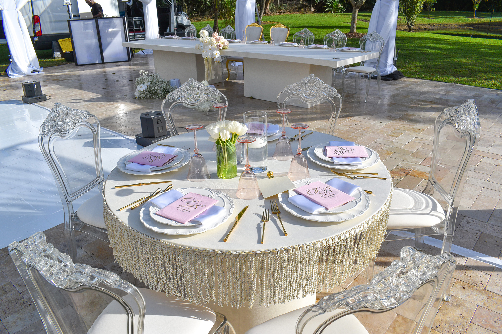 Round reception table with fringed linen, blush programs, and clear chairs at Saint Patrick Palace.