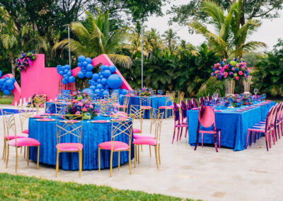 Vivid pink & blue outdoor party setup with luxe decor, balloon backdrop, and vibrant floral arrangements.