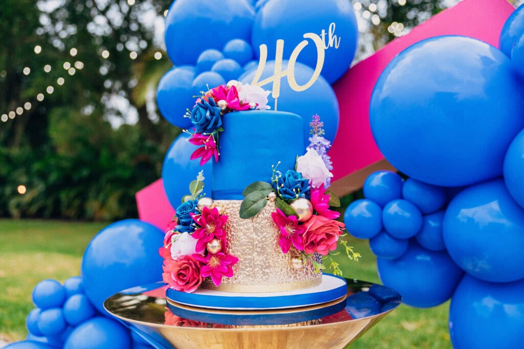 Bold blue & gold 40th birthday cake with pink florals – perfect for luxury milestone celebrations outdoors.