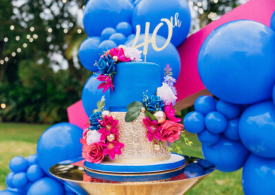 Bold blue & gold 40th birthday cake with pink florals – perfect for luxury milestone celebrations outdoors.