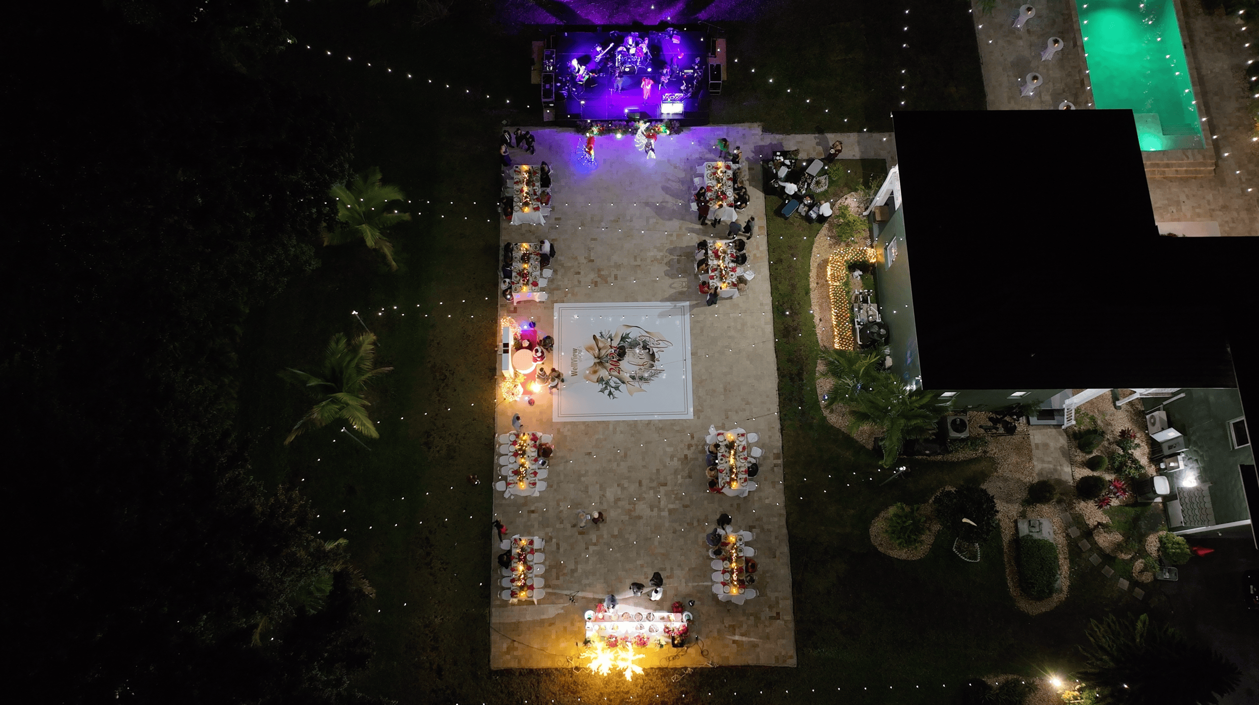 Overhead view of a corporate holiday party with banquet tables, a dance floor, live band, and illuminated pool.