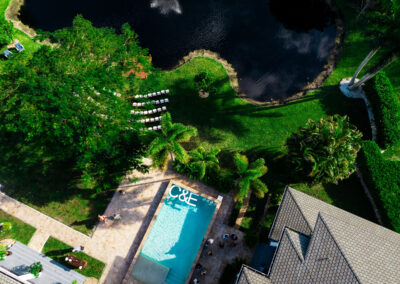 Aerial view of luxury estate wedding with poolside reception and lakeside ceremony setup.