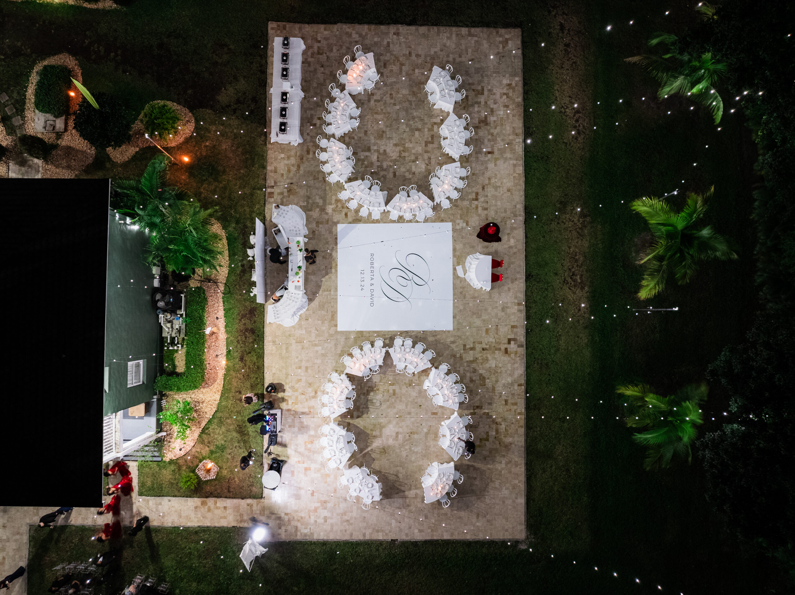 Outdoor Airbnb-style wedding reception at Saint Patrick Palace with bistro lights and round tables around a monogrammed dance floor.