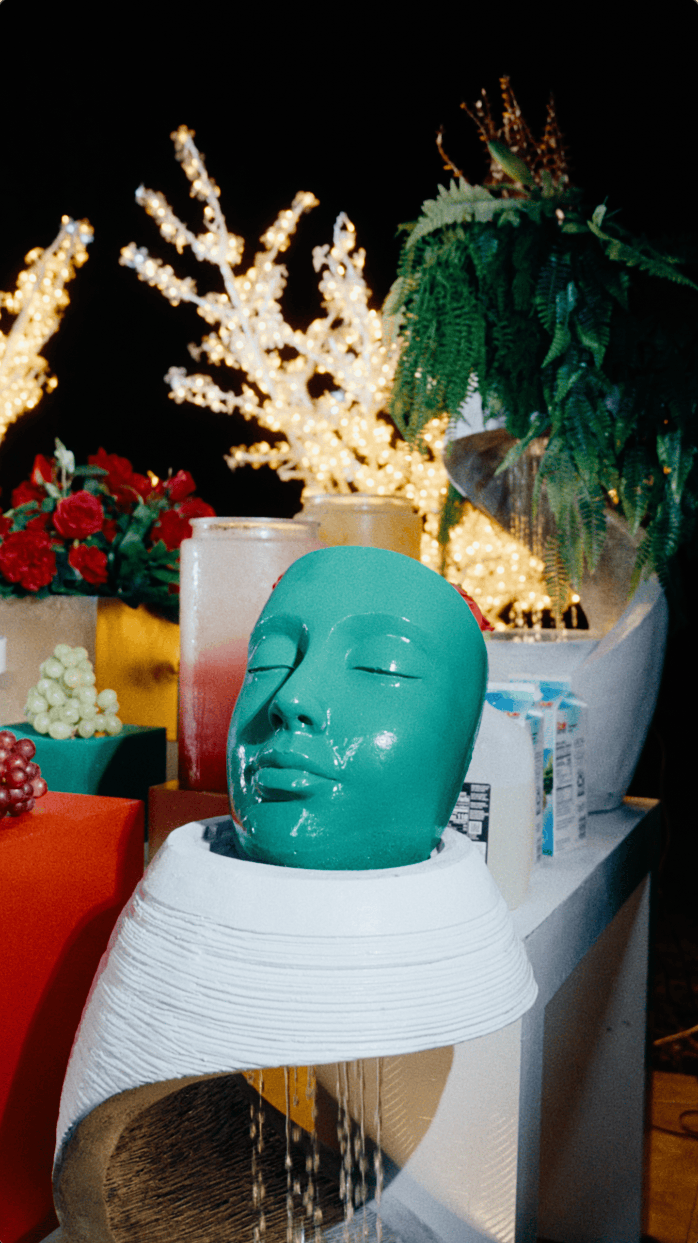 Glossy emerald-green face sculpture surrounded by illuminated branches and festive holiday buffet decorations.