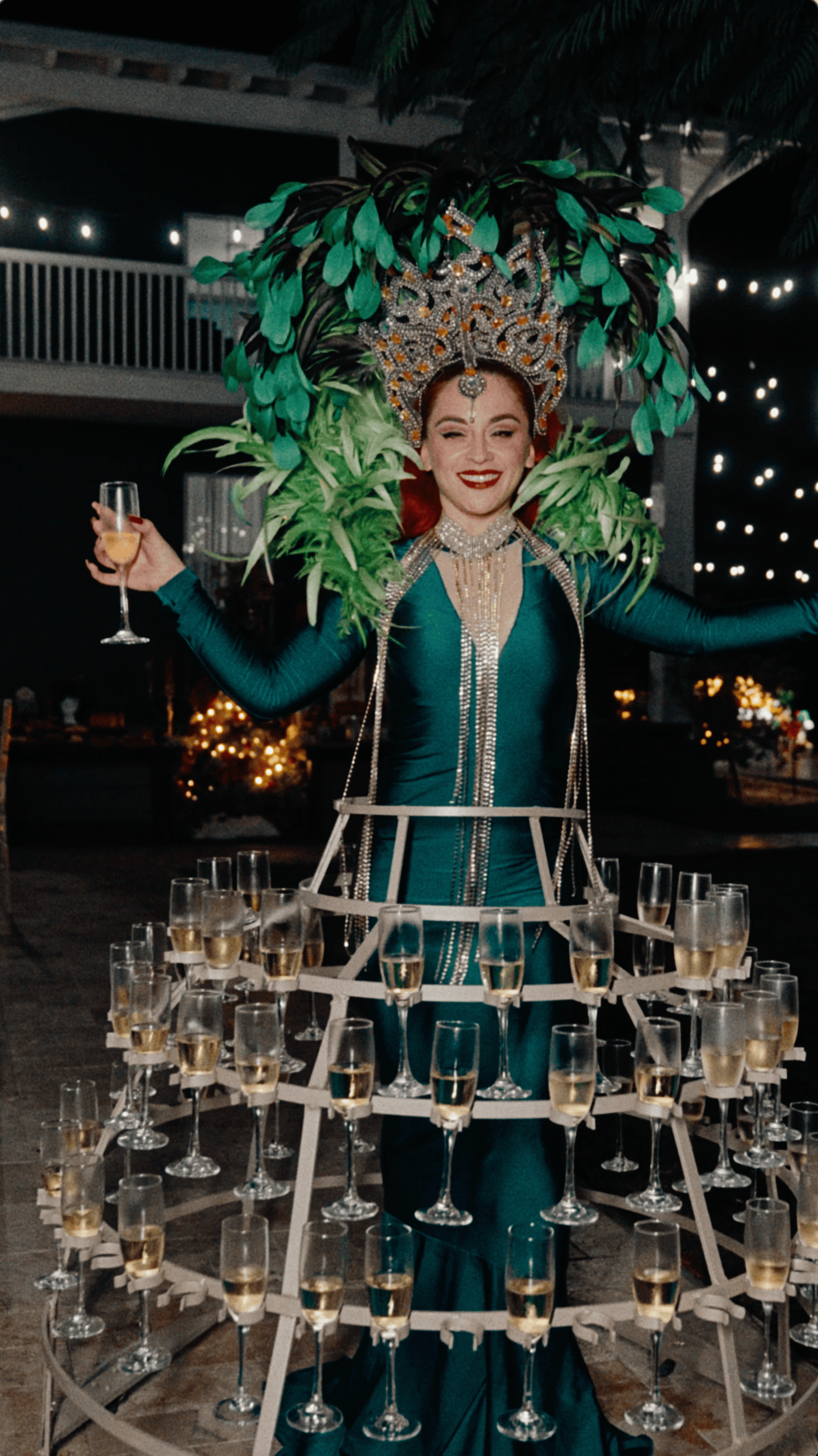Champagne skirt performer in an emerald-green gown and jeweled headdress surrounded by champagne flutes.