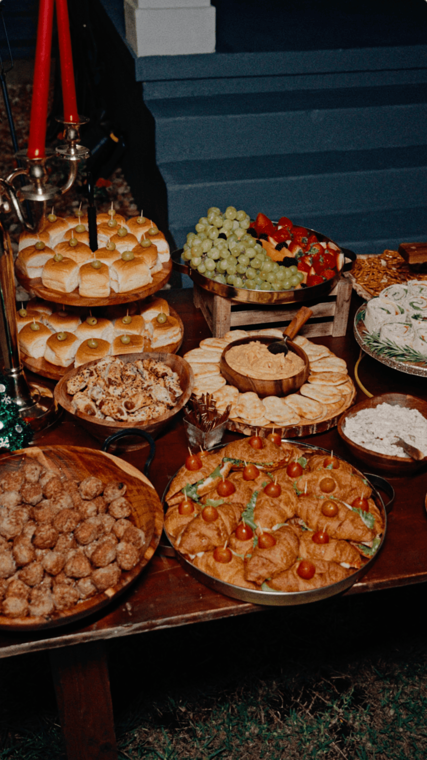 Outdoor Christmas appetizer buffet with mini sandwiches, fresh fruit, crackers, dips, and savory pastries.