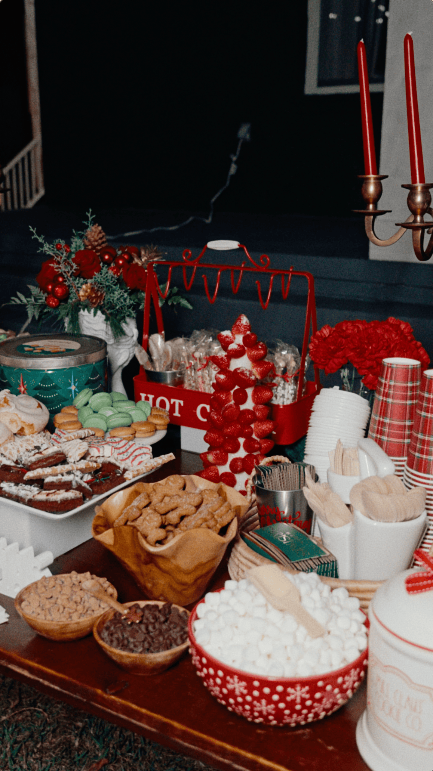 Christmas hot chocolate station with marshmallows, holiday desserts, cookies, and a strawberry centerpiece.