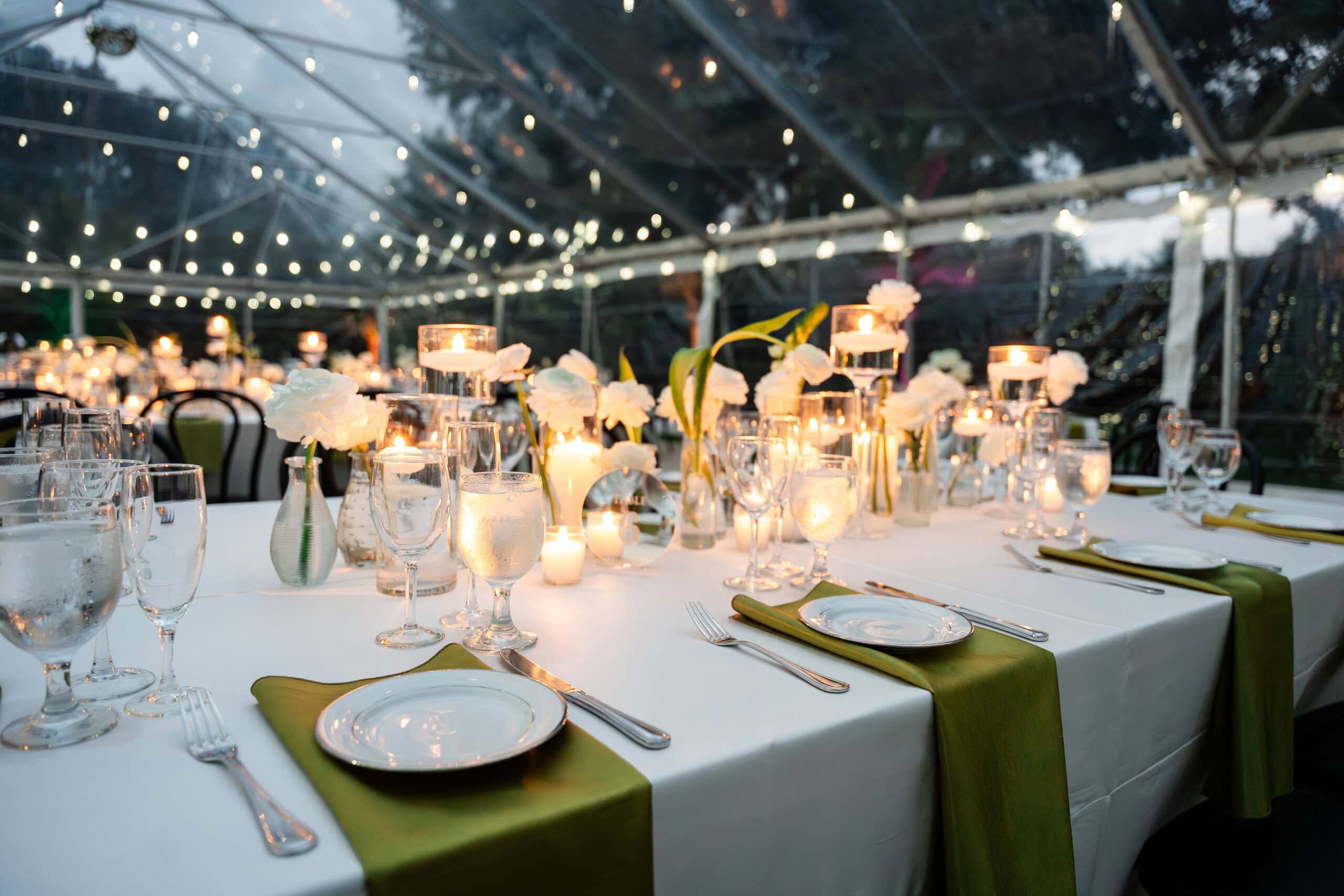 Candlelit wedding reception beneath a clear top tent at Saint Patrick Palace with elegant floral centerpieces and bistro lighting.