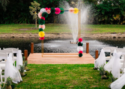 Colorful paper fan arch and pineapple décor by the pond