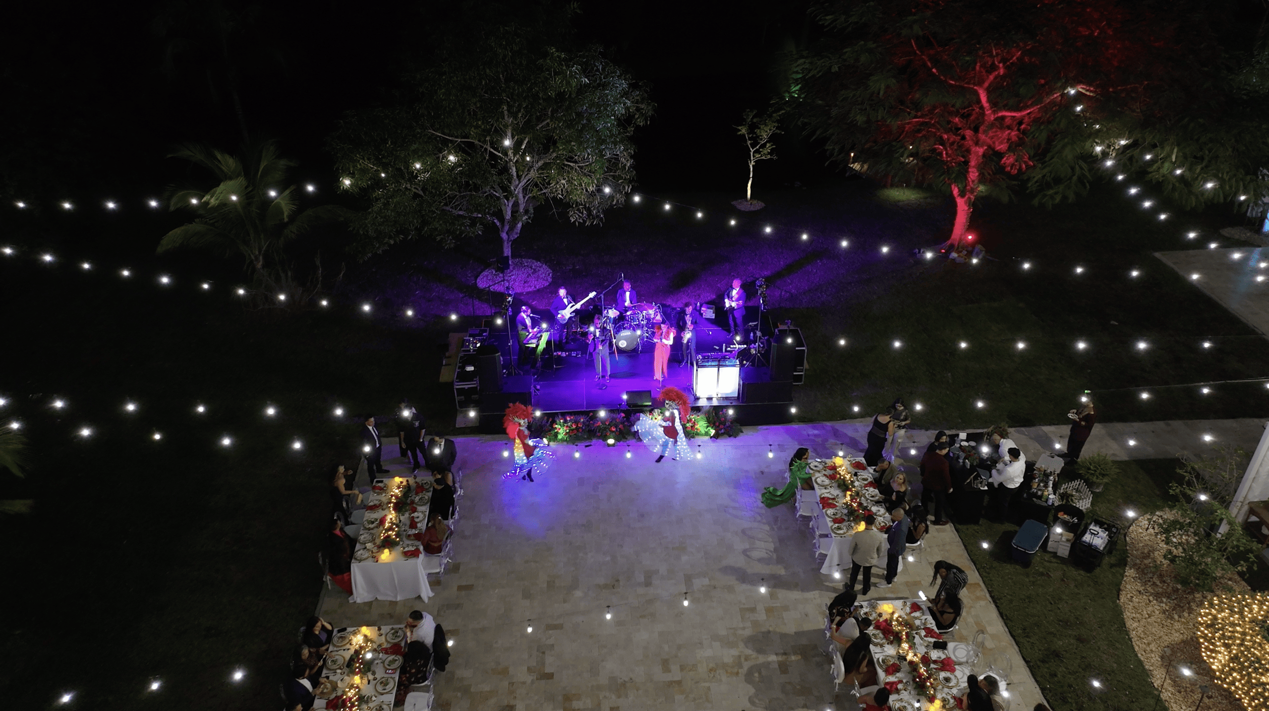 A live band performs at an outdoor holiday party with festive banquet tables and string lights at Saint Patrick Palace.