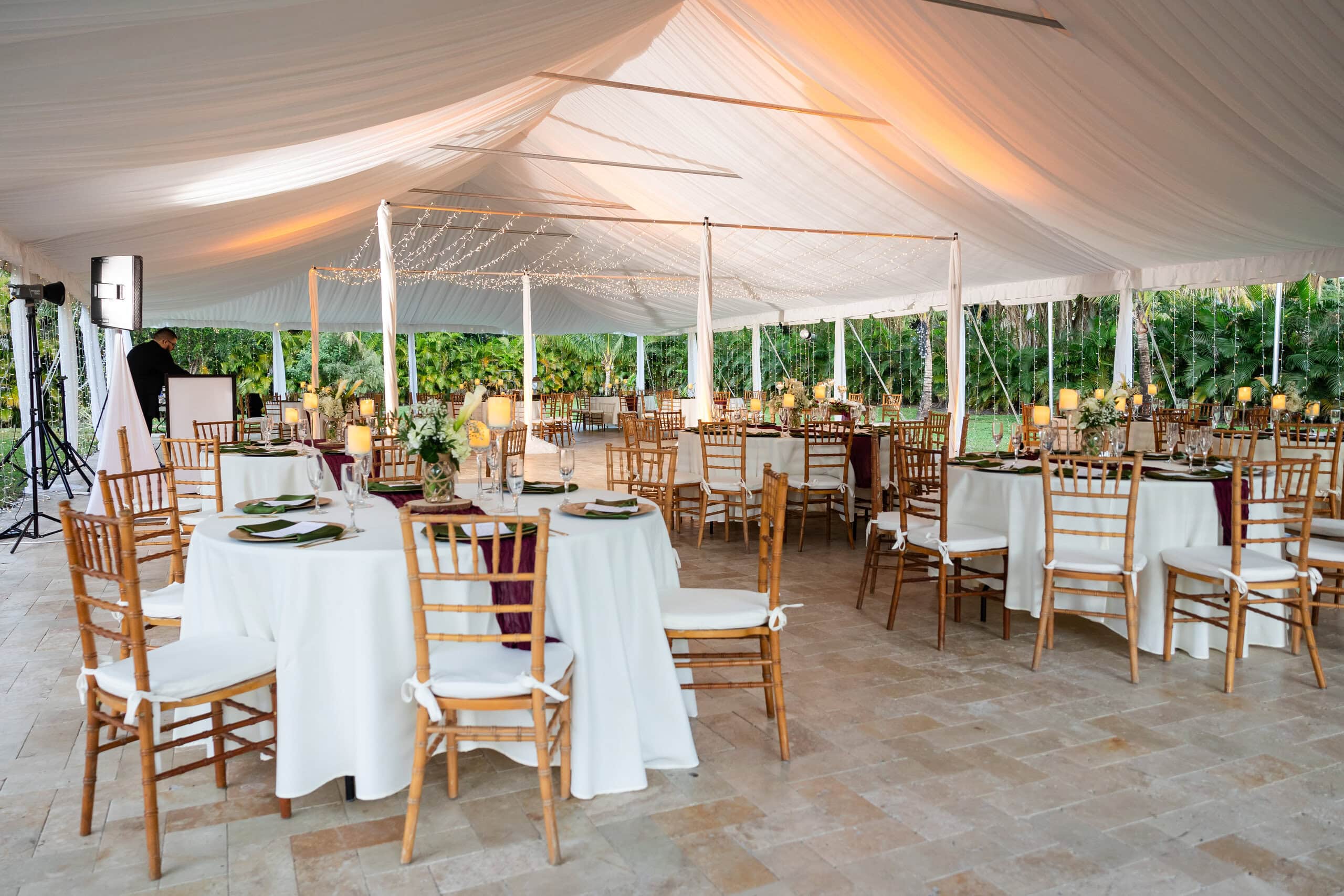 Covered outdoor wedding reception with white draped tent, round tables, gold chairs, and open sides at Saint Patrick Palace.