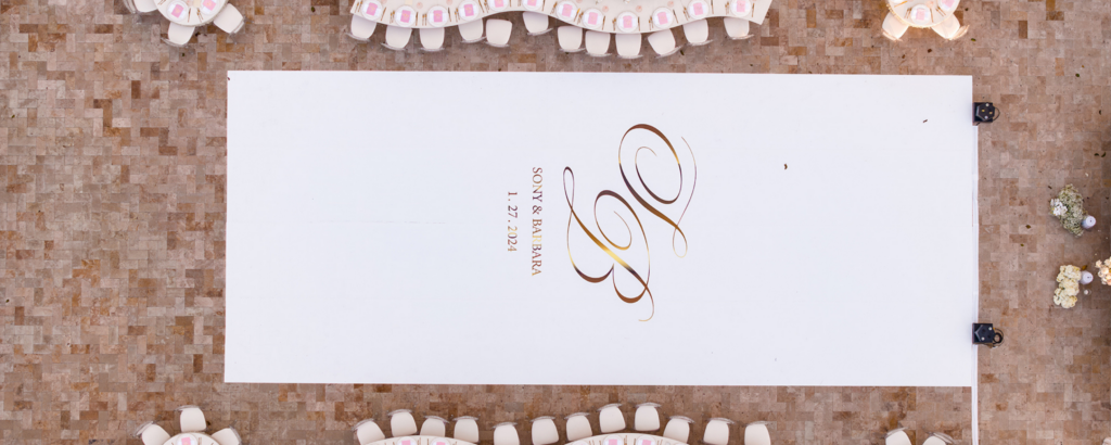 Overhead view of a custom white dance floor with gold monogram "Sony & Barbara" on a paved terrace.