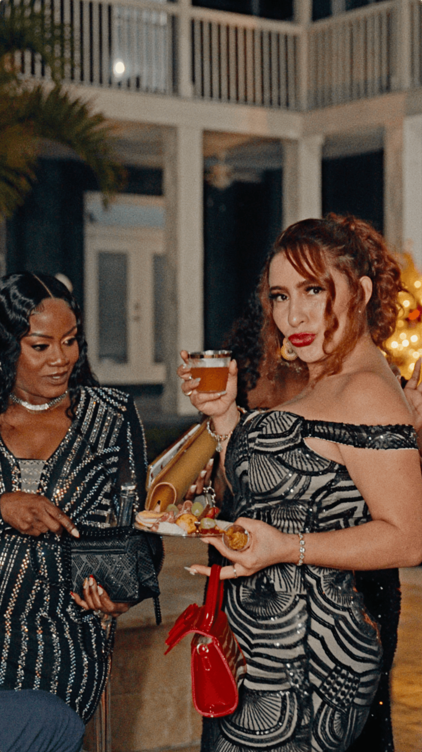 Two elegantly dressed guests enjoying drinks and appetizers at an outdoor holiday party in Davie, Florida.