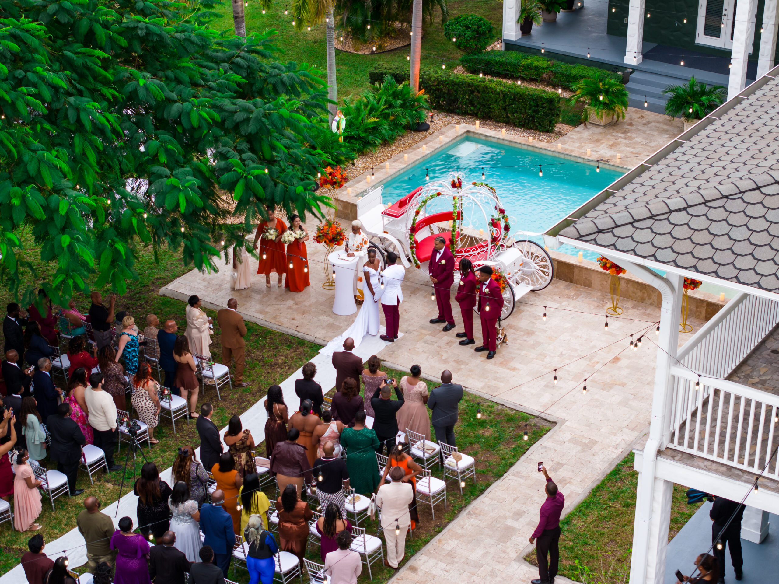 Elegant outdoor wedding ceremony by the pool with white carriage décor at a luxury private estate.