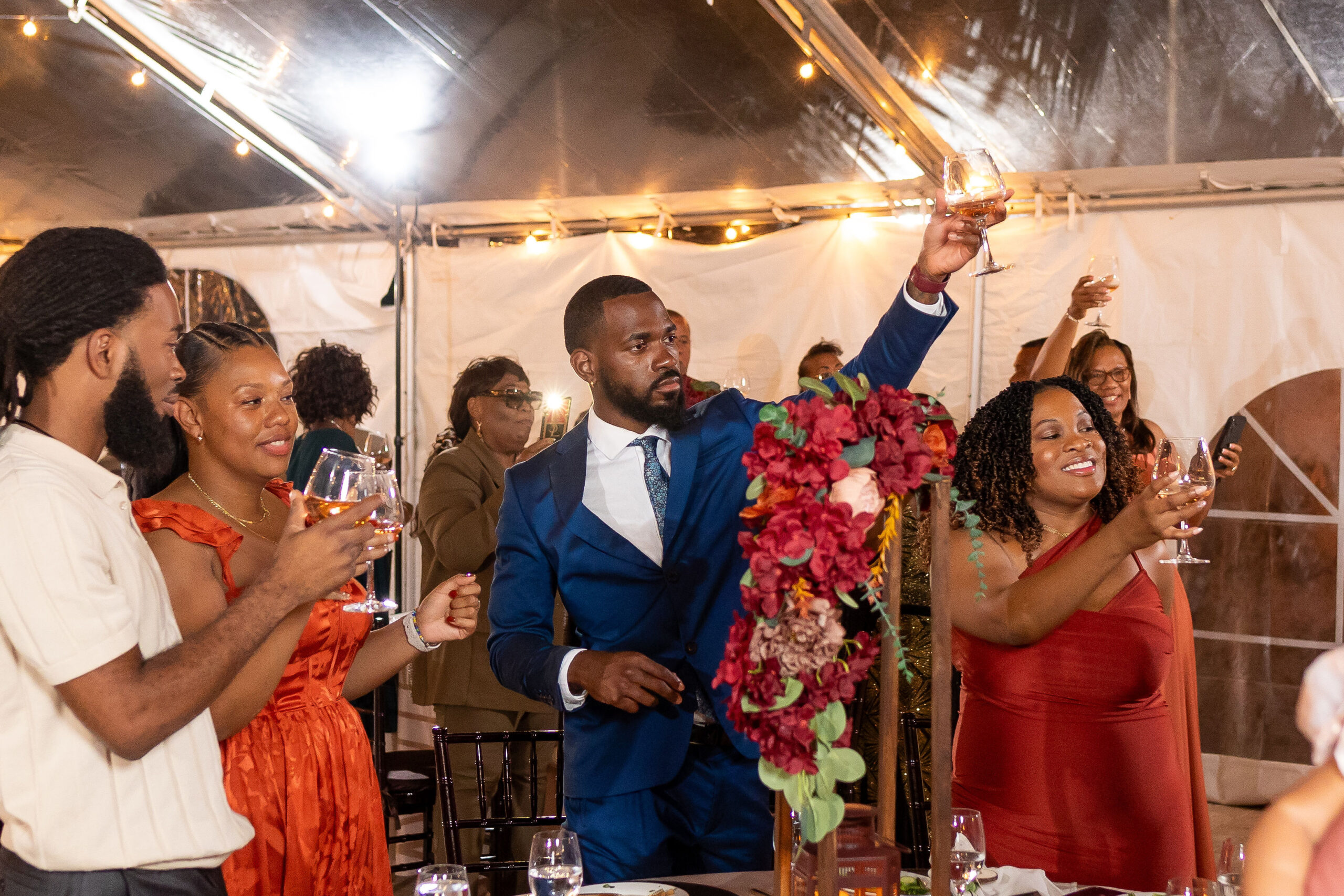 Guests raising glasses in a joyful toast at an elegant retirement party under a decorated tent.