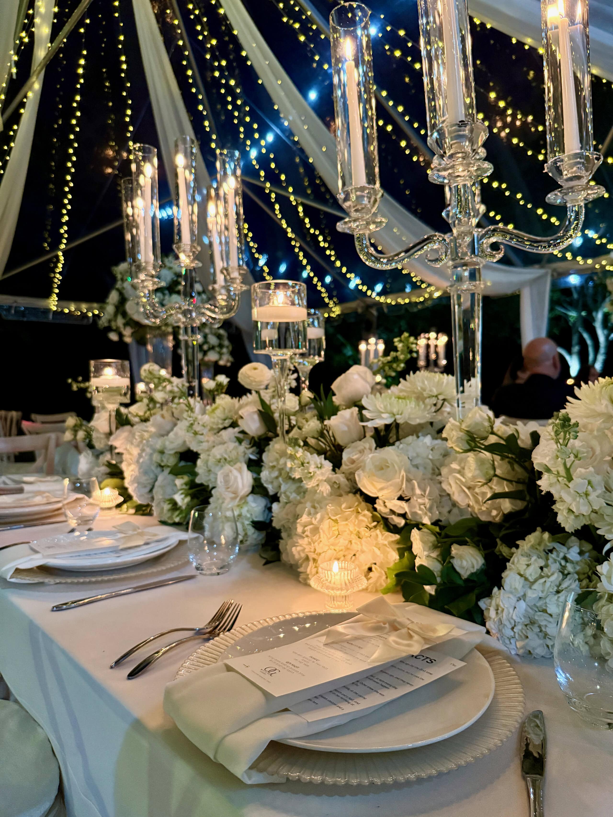 Elegant candlelit wedding reception table with white floral centerpieces and string lights at Saint Patrick Palace
