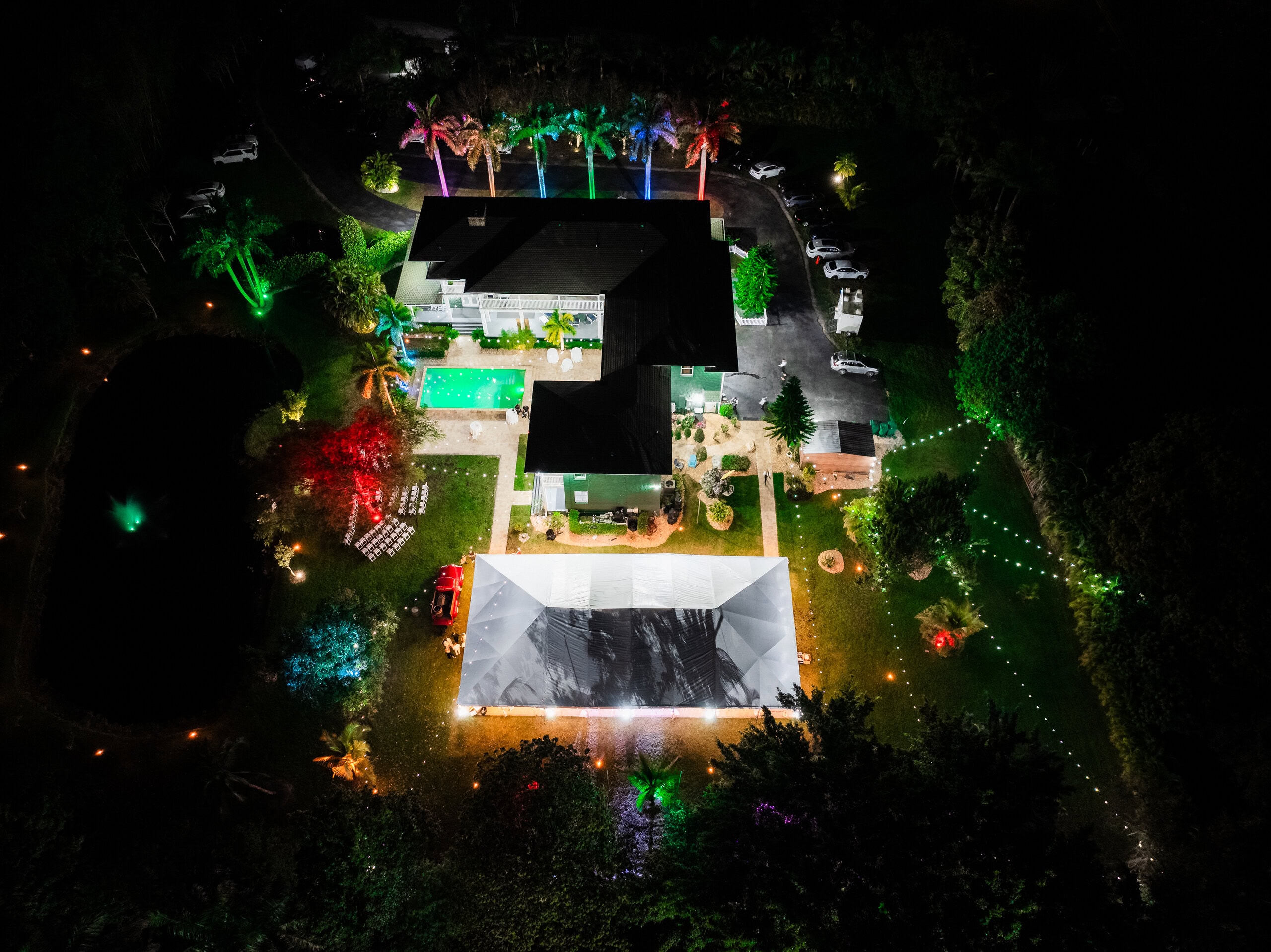 Nighttime aerial of Saint Patrick Palace showing a covered wedding reception tent, illuminated pool, residence, and gardens.