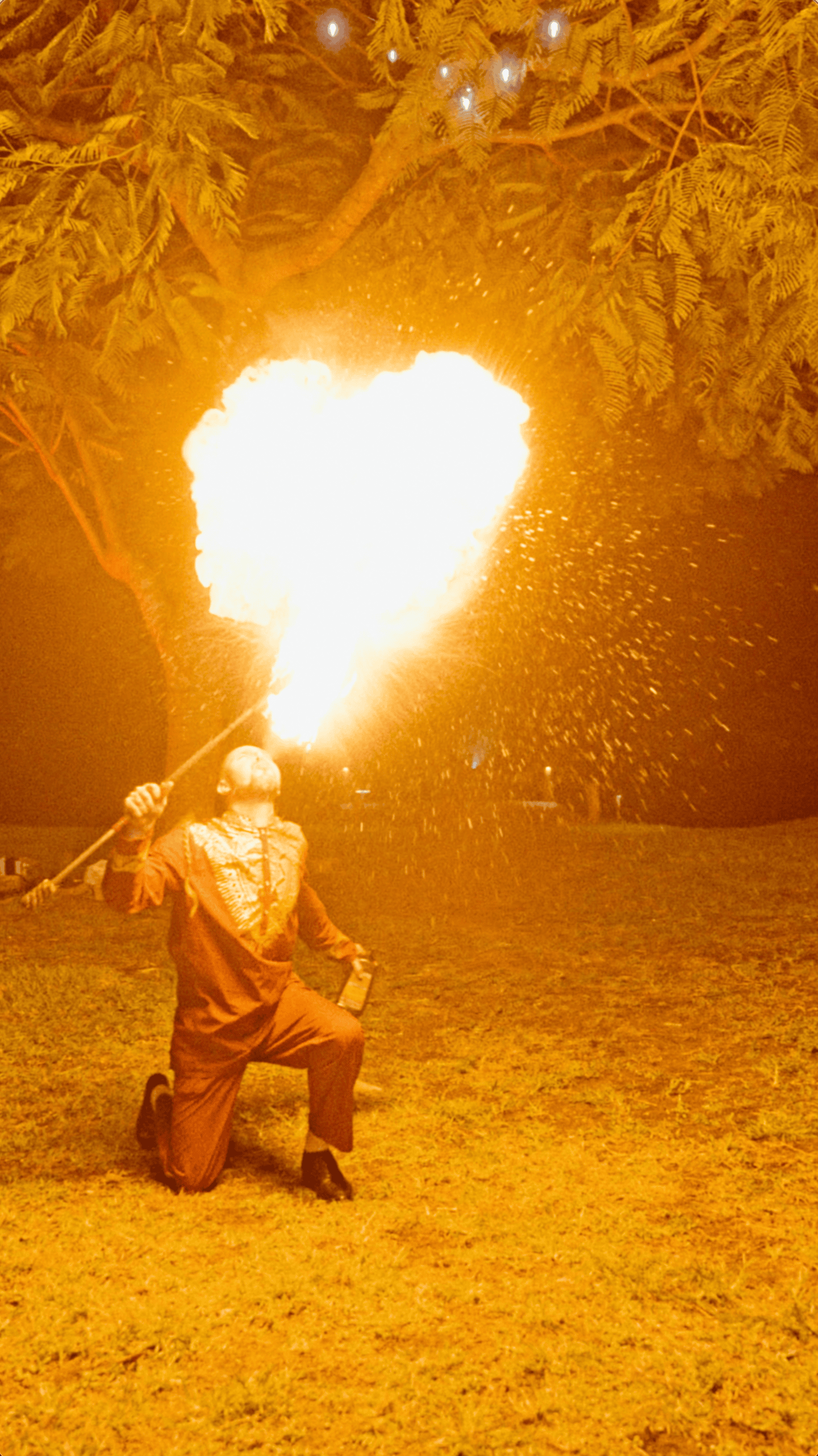 Fire performer creating a dramatic burst of flame during an outdoor nighttime holiday celebration.