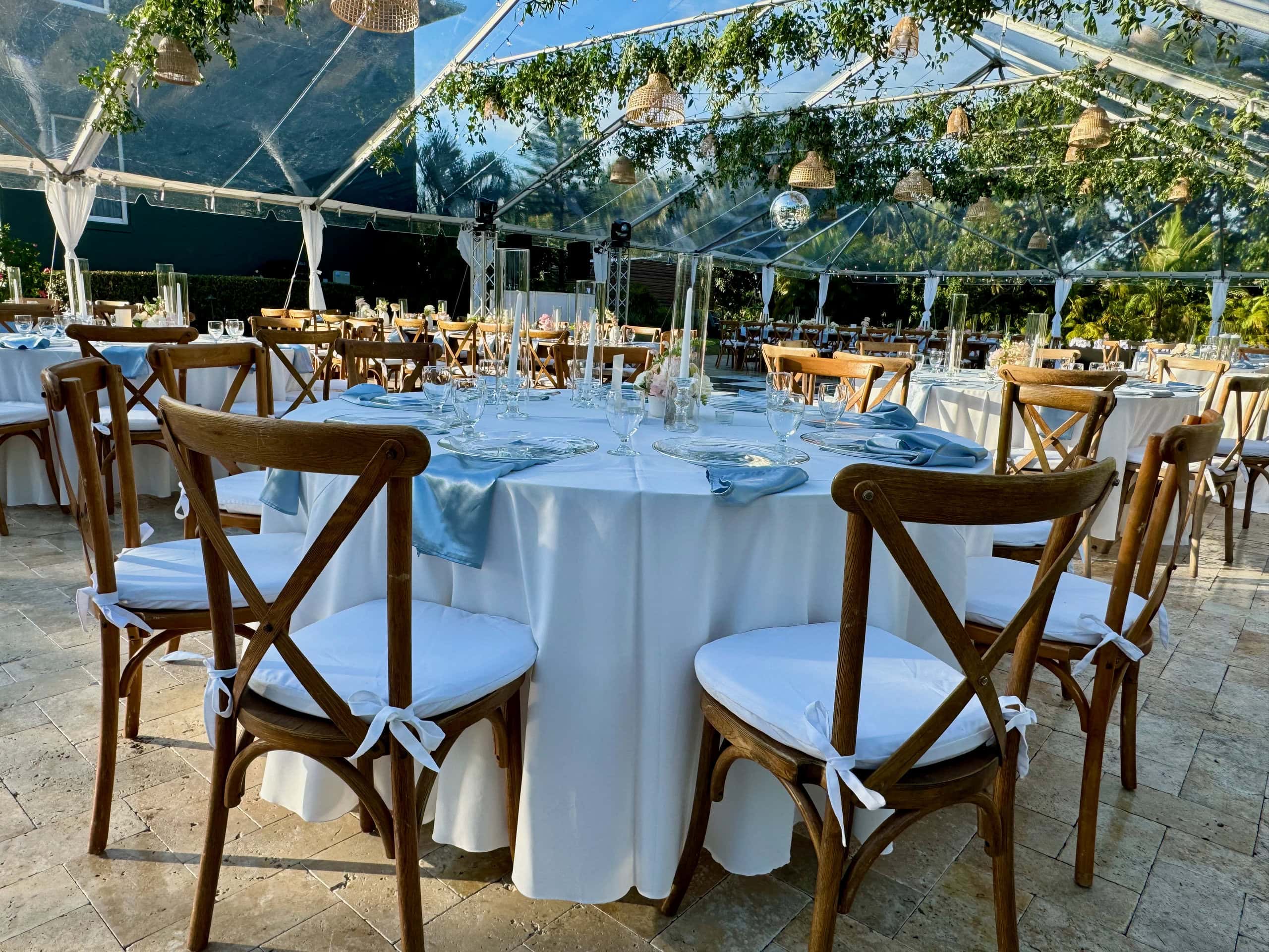 Garden tent wedding table with white linens and cross-back chairs under clear tent