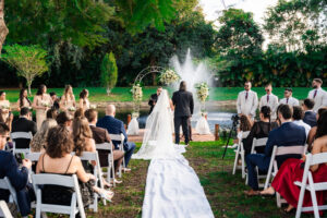 Bride walking down a white aisle runner toward a floral arch at an outdoor wedding ceremony.