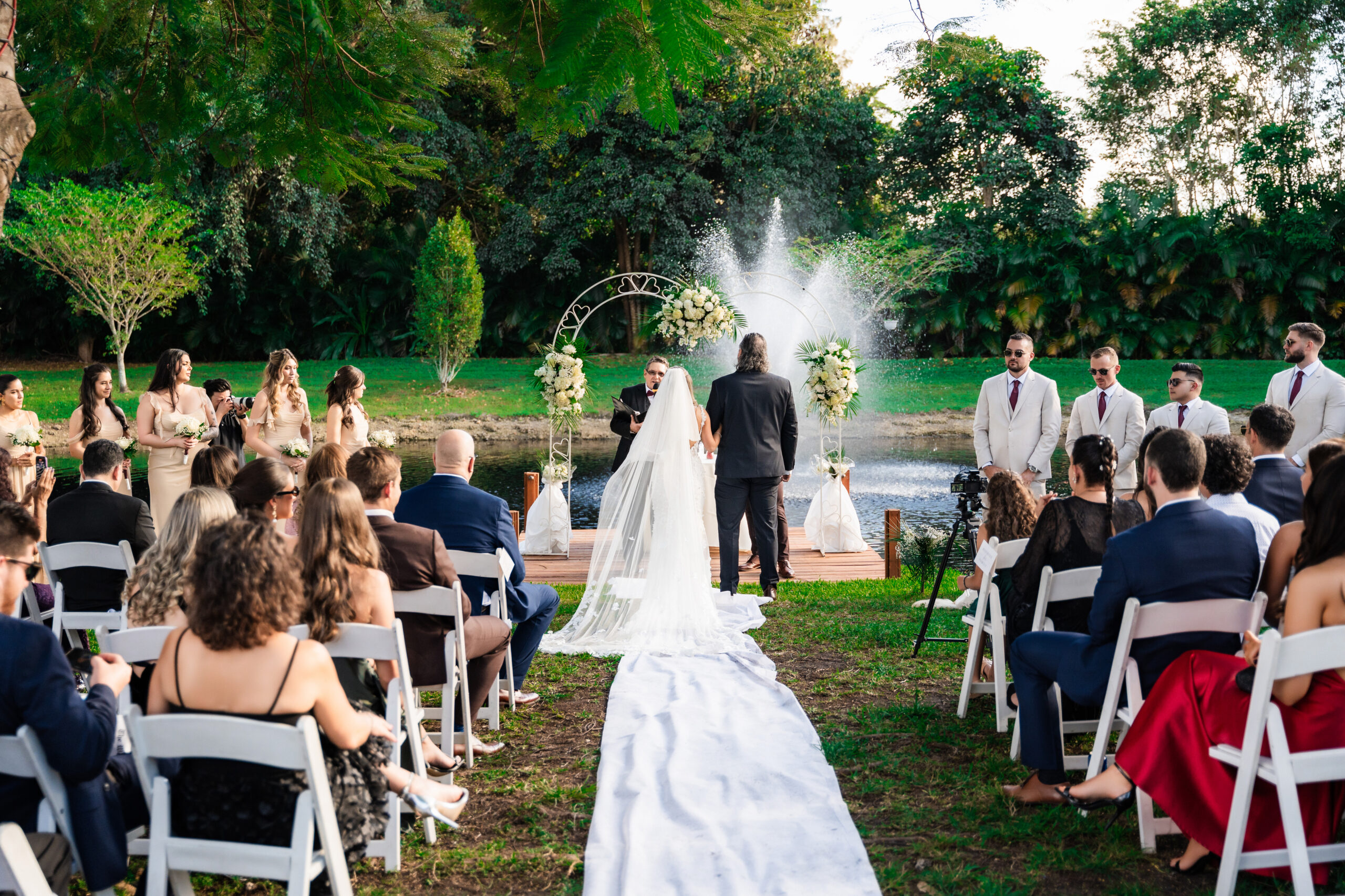 Bride walking down a white aisle runner toward a floral arch at an outdoor wedding ceremony.