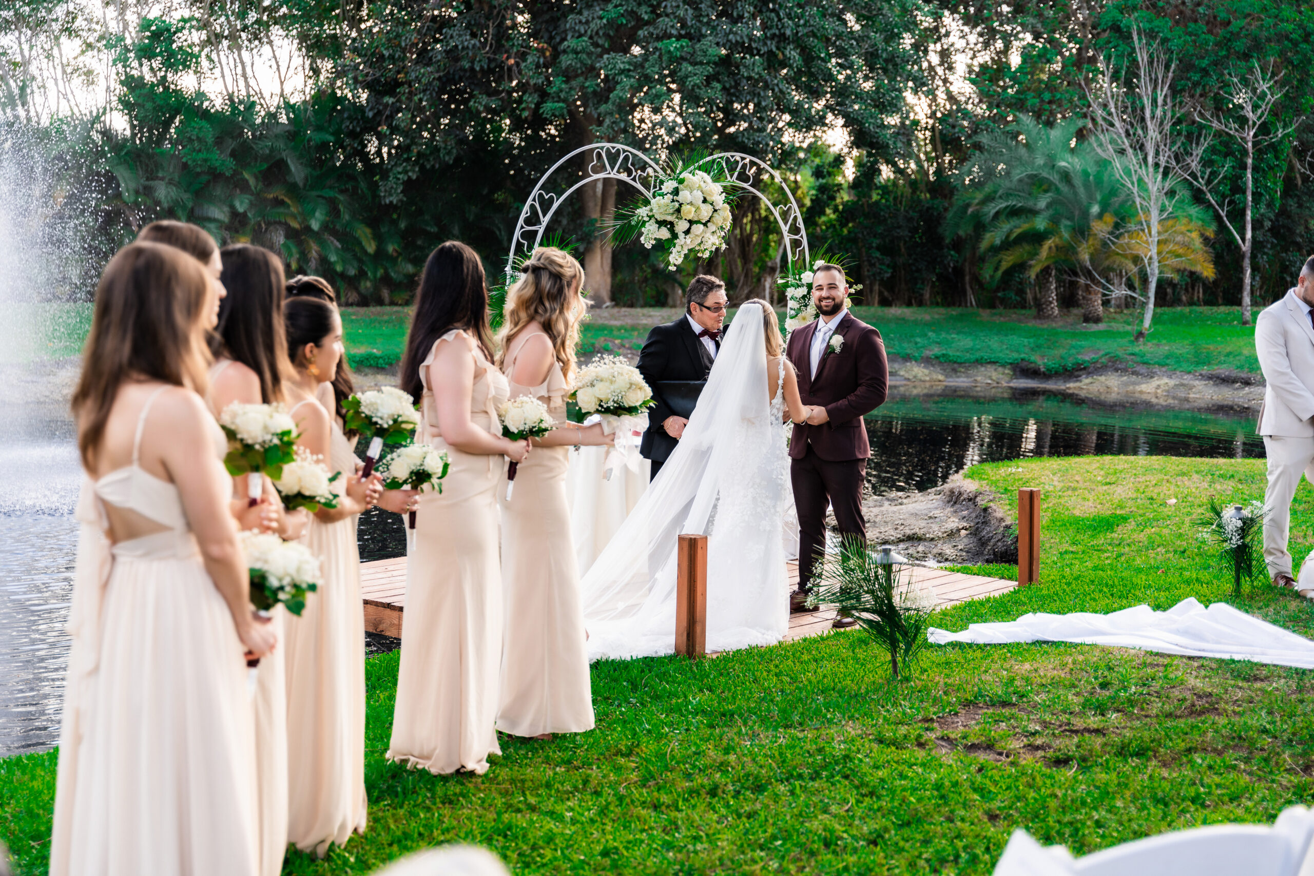 Bride and groom at the altar with bridesmaids lined up beside the pond and fountain at Saint Patrick Palace.