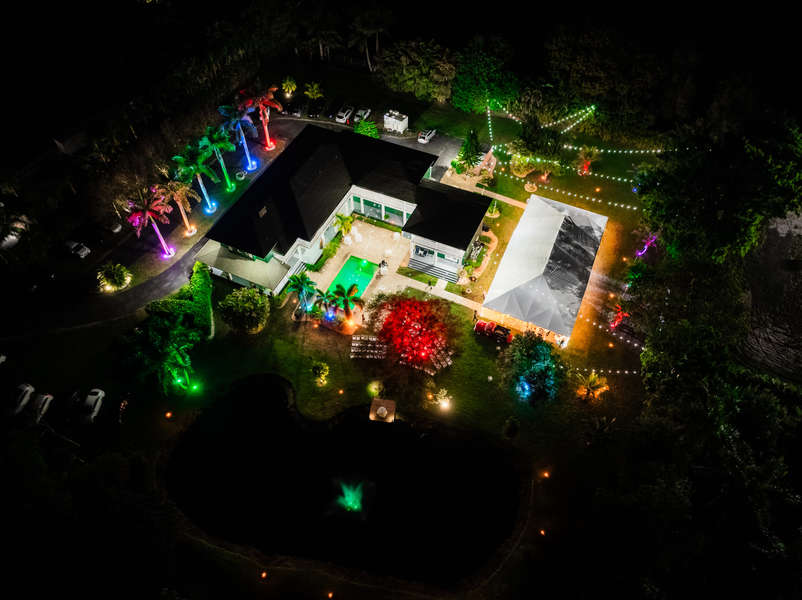 Aerial night view of Saint Patrick Palace with colorful uplighting, tent, and pond fountain.