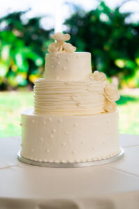 Three-tier white buttercream wedding cake with dot details and floral accents on a reception table.