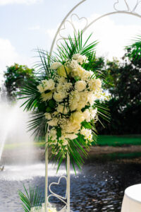 Close-up of white roses and greenery on a ceremony arch beside a pond at Saint Patrick Palace.