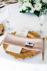 Gold charger with champagne napkin, custom menu card, and white floral centerpiece at a wedding reception table.